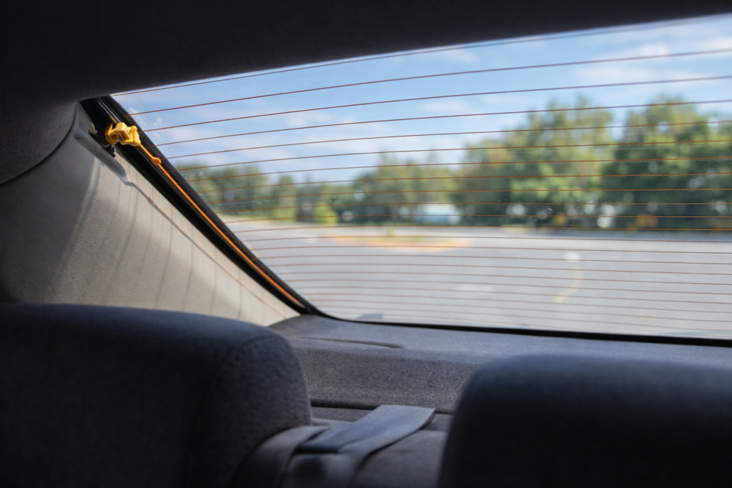 Rear windshield AM antenna grid lines visible from inside car with connection point near pillar in natural daylight.

