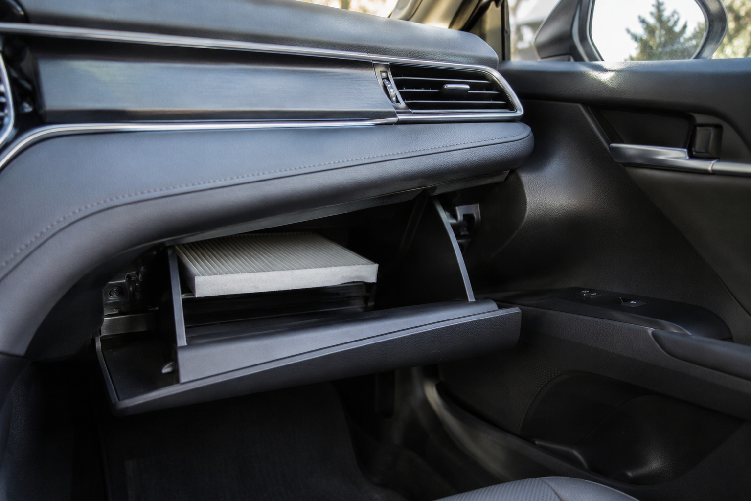 Toyota Camry cabin air filter location behind glove box during DIY replacement with clean automotive interior view